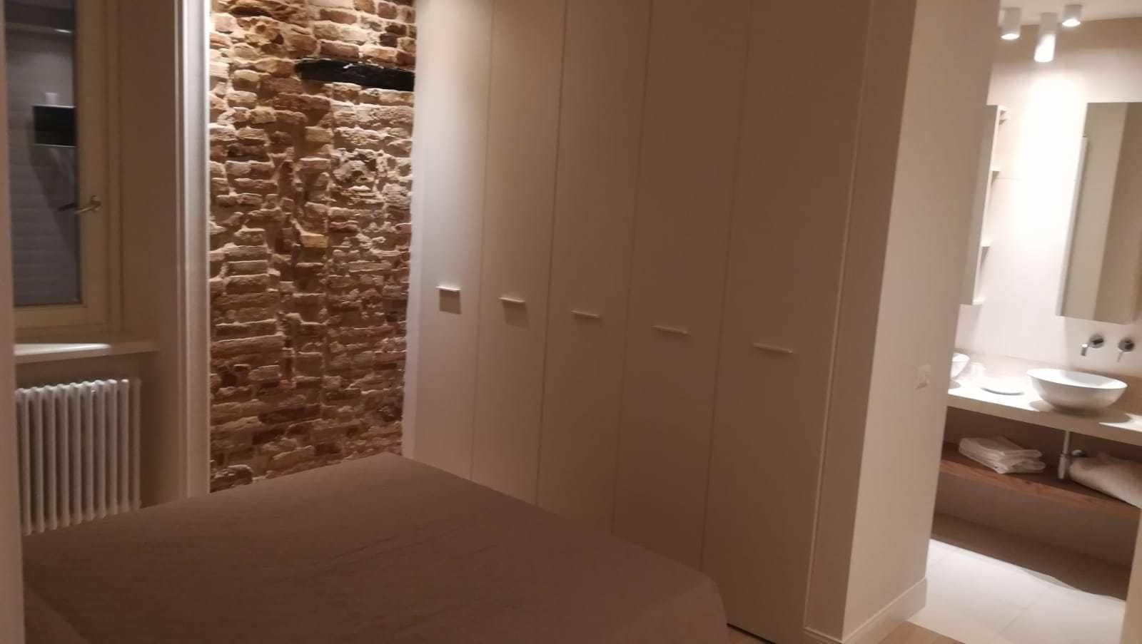 Un dormitorio con pared de piedra, un armario y un baño con lavabo y espejo.