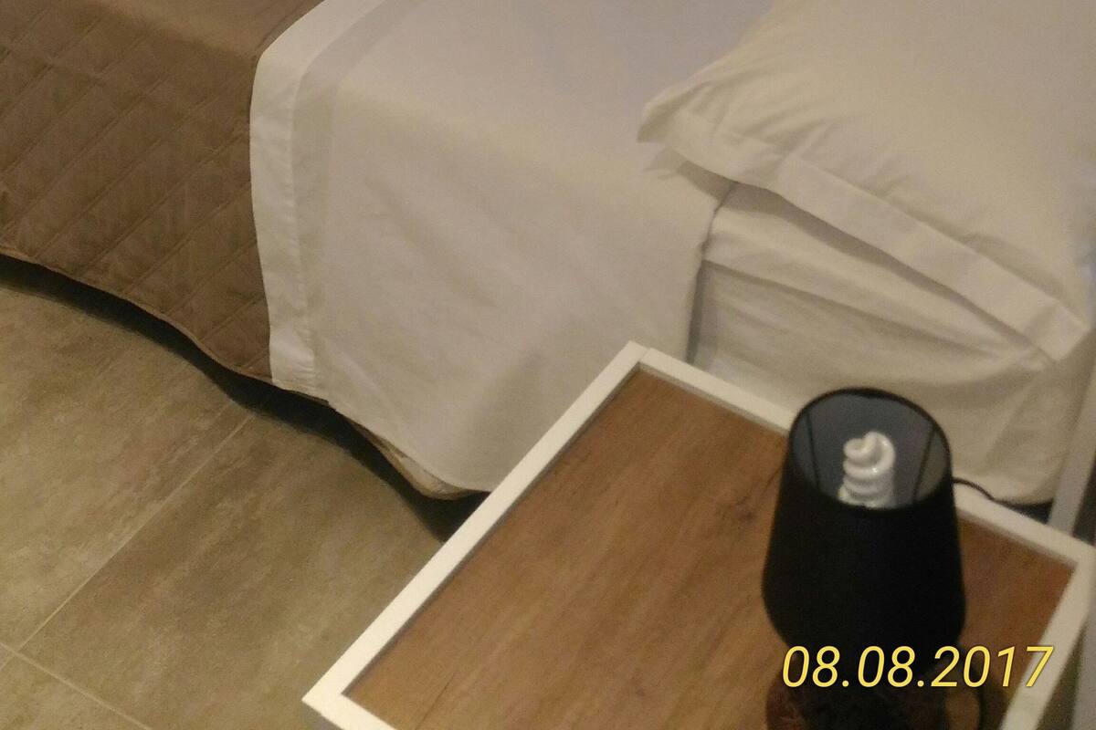 Una stanza con parete in pietra, un letto con biancheria bianca, un comodino in legno e una lampada.