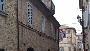 Un carrer empedrat i estret flanquejat per edificis històrics de maó, amb un bar anomenat "BAR Edicola" i una escala visible que condueix a un nivell superior.