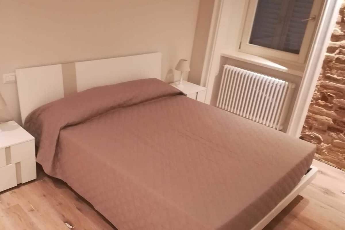 Una camera da letto con un letto, un comodino, una lampada e una finestra vista un muro in pietra.
