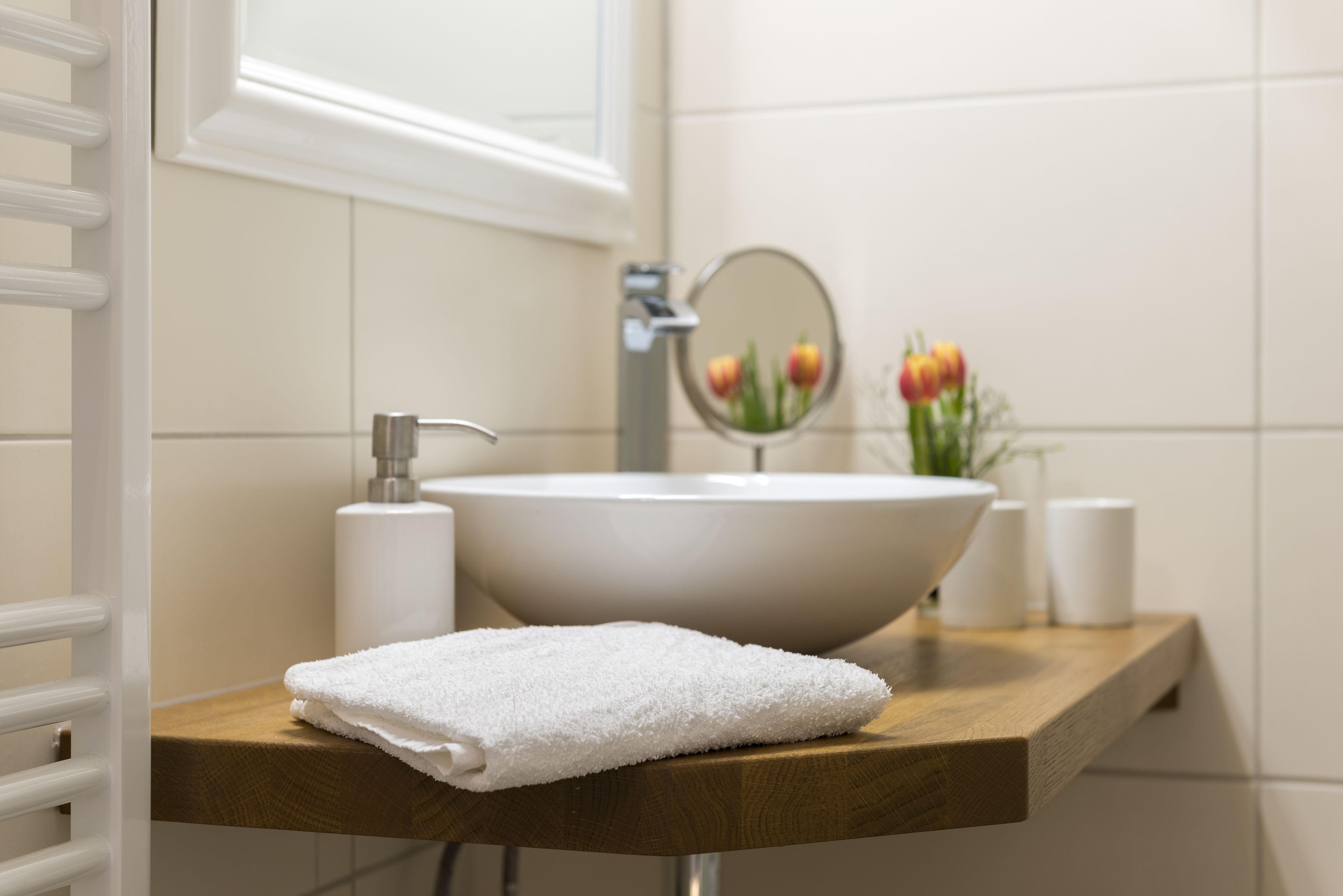 A bathroom with a white sink, a wooden countertop, a towel, a mirror, and a vase with flowers.