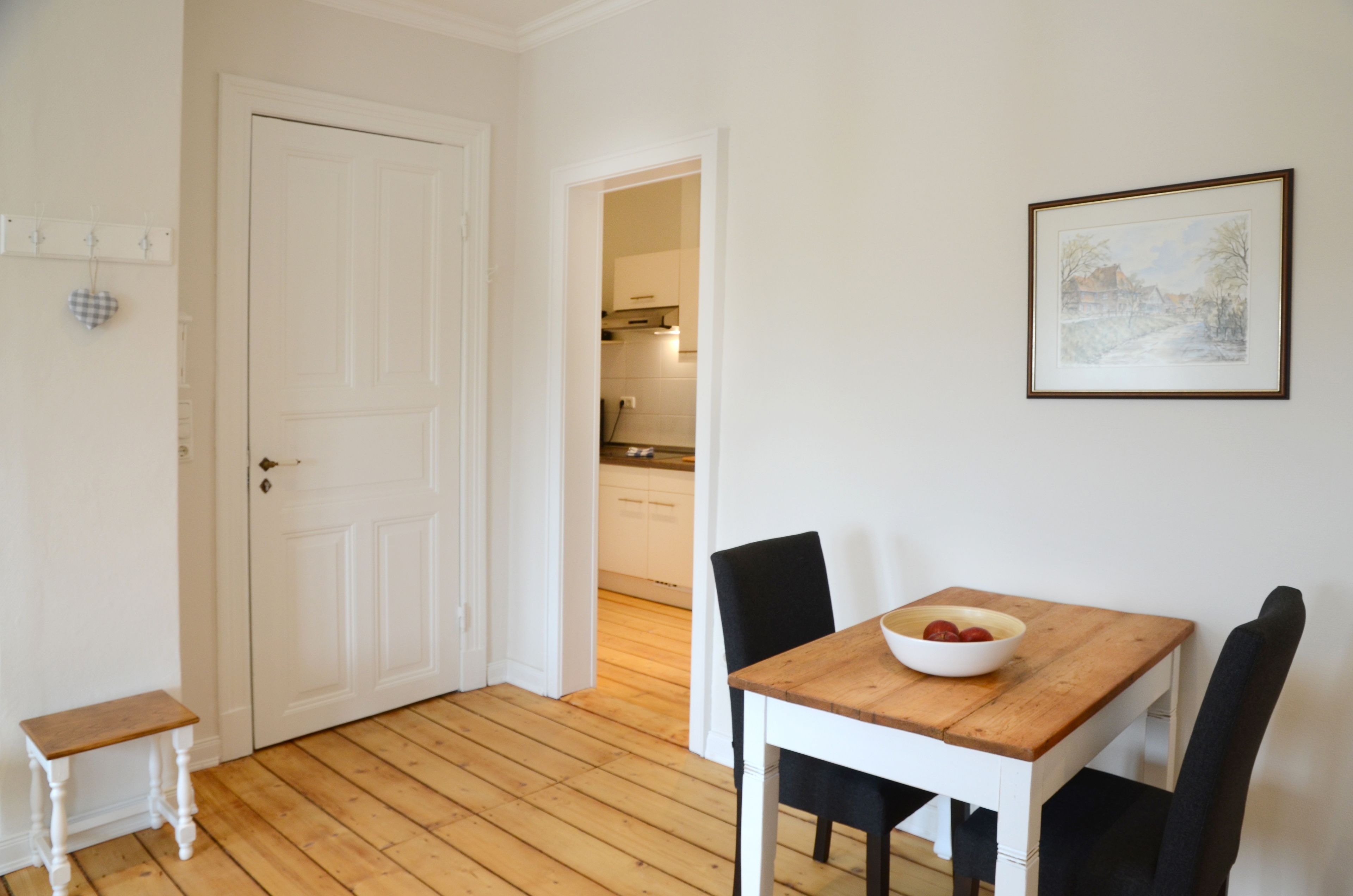 Een eethoek met een houten tafel en stoelen, een witte deur en een lijst met een afbeelding aan de muur.