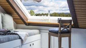A cozy attic bedroom with a skylight, a wooden chair, and a cushioned bench. - Urlaub Hamburg Altes Land (Hamburg)