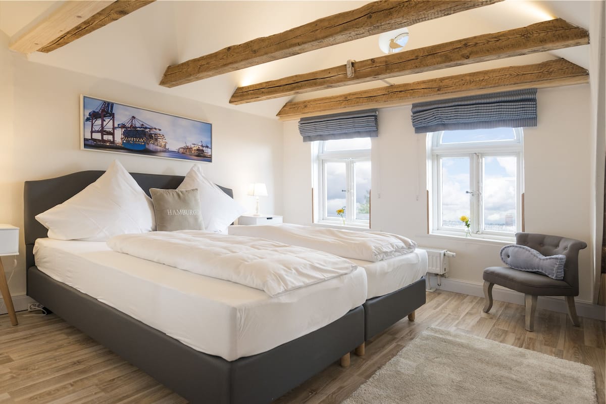 A bedroom with a large bed, wooden beams, a window with a view, and a painting on the wall.