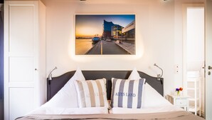 A neatly made bed with two pillows, a framed cityscape picture above it, and a small bedside table with a vase of flowers. - Urlaub Hamburg Altes Land (Hamburg)