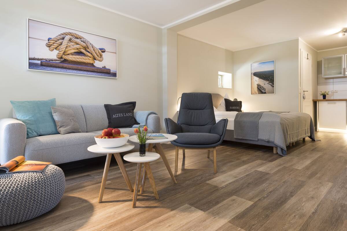 A modern living room with a sofa, armchair, and a small table with a bowl of fruit and flowers.