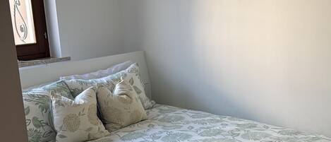 A bedroom with a bed, pillows, a painting of a beach scene, and a window with curtains.