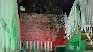 Une piscine dont l’eau est illuminée de lumière verte, entourée d’un mur de briques et d’une balustrade blanche.