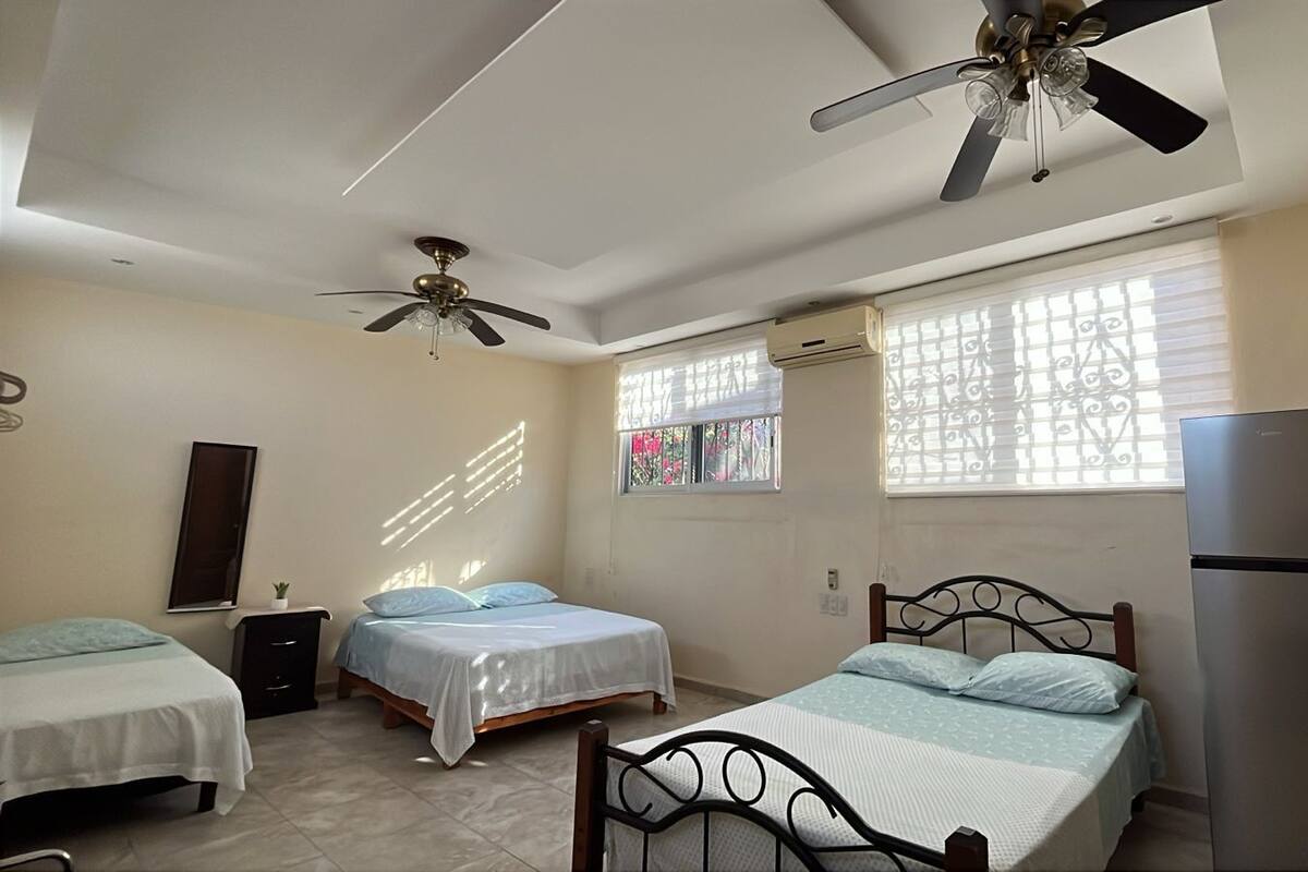A bedroom with two beds, a ceiling fan, a refrigerator, and a window with decorative bars.