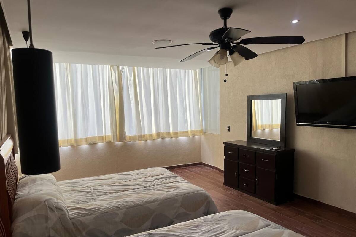 A hotel room with two beds, a ceiling fan, a TV, and a dresser.