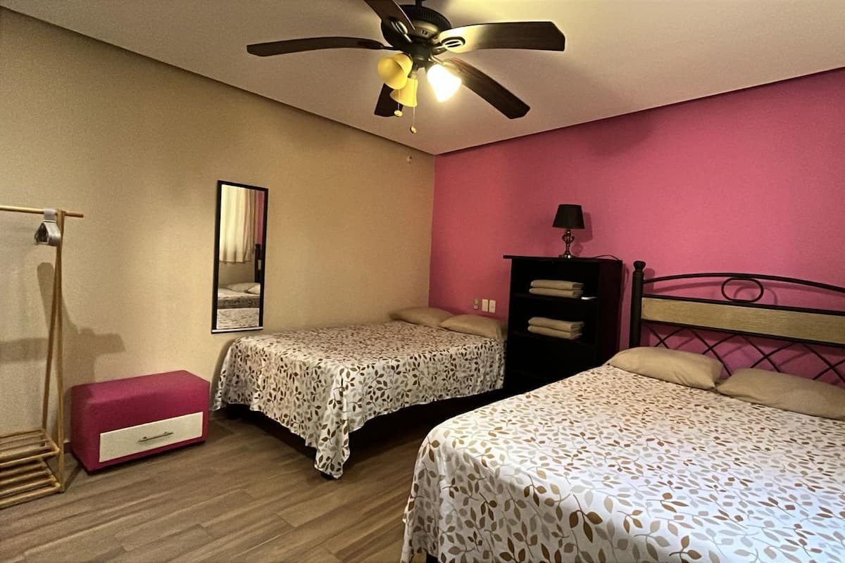 A bedroom with two beds, a ceiling fan, a wardrobe, and a bedside table.
