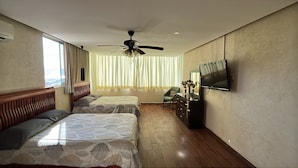 Une chambre d’hôtel avec deux lits, un ventilateur de plafond, une télévision et une vue sur la ville grâce à de grandes fenêtres.