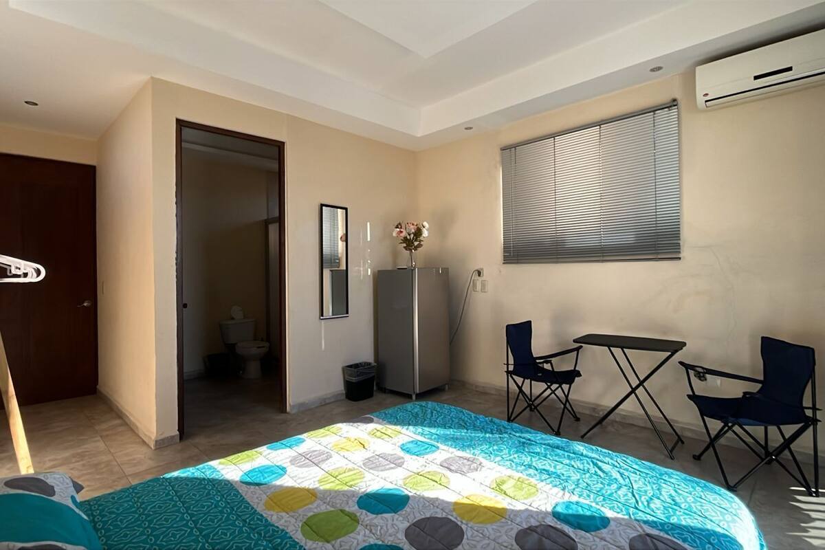 A bedroom with a bed, a desk, two chairs, a wardrobe, and a window with blinds.