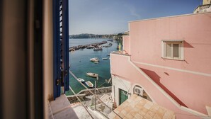 A coastal view with boats docked at a pier, a pink building with a window, and a clear sky. - Corricella Sea Window (Procida)