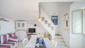 A cozy living area with a sofa, a dining table set with a blue table runner, and a staircase leading to a bedroom. - Corricella Sea Window (Procida)