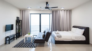 A modern hotel room with a large bed, a sofa, a TV, a bookshelf, and a balcony with curtains. - Miko's Home (Shah Alam)
