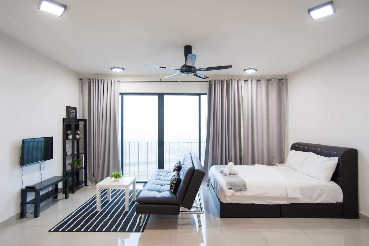 A modern hotel room with a large bed, a sofa, a TV, a bookshelf, and a balcony with curtains.