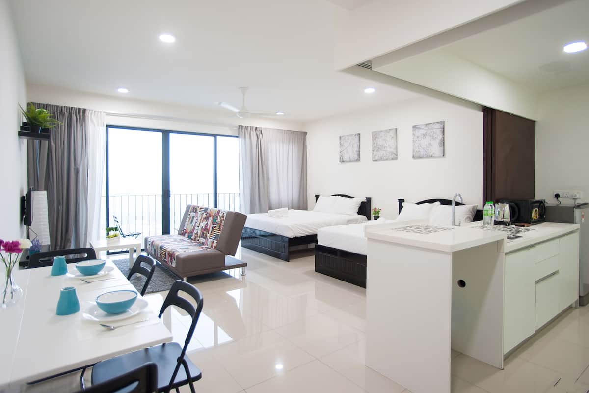A modern hotel room with a dining area, two beds, a kitchenette, and large windows with curtains.