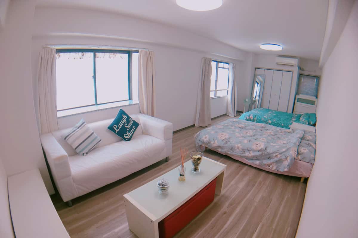 Ein modernes Schlafzimmer mit einem weißen Sofa, einem Bett mit floralem Bettzeug, einem kleinen weißen Tisch und einem roten Schrank.
