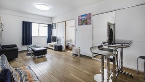 A modern hotel room with a wooden floor, a flat-screen TV, a bed, a desk, and a chair. - Shinsaibashi Su Casa Apartment (Osaka)