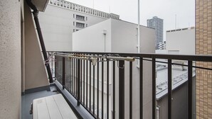 A balcony with a metal railing, a white door, and a view of adjacent buildings. - Shinsaibashi Su Casa Apartment (Osaka)