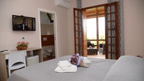 Una camera d'albergo con un letto, una scrivania con un computer, una TV e un bagno visibile attraverso una porta aperta.