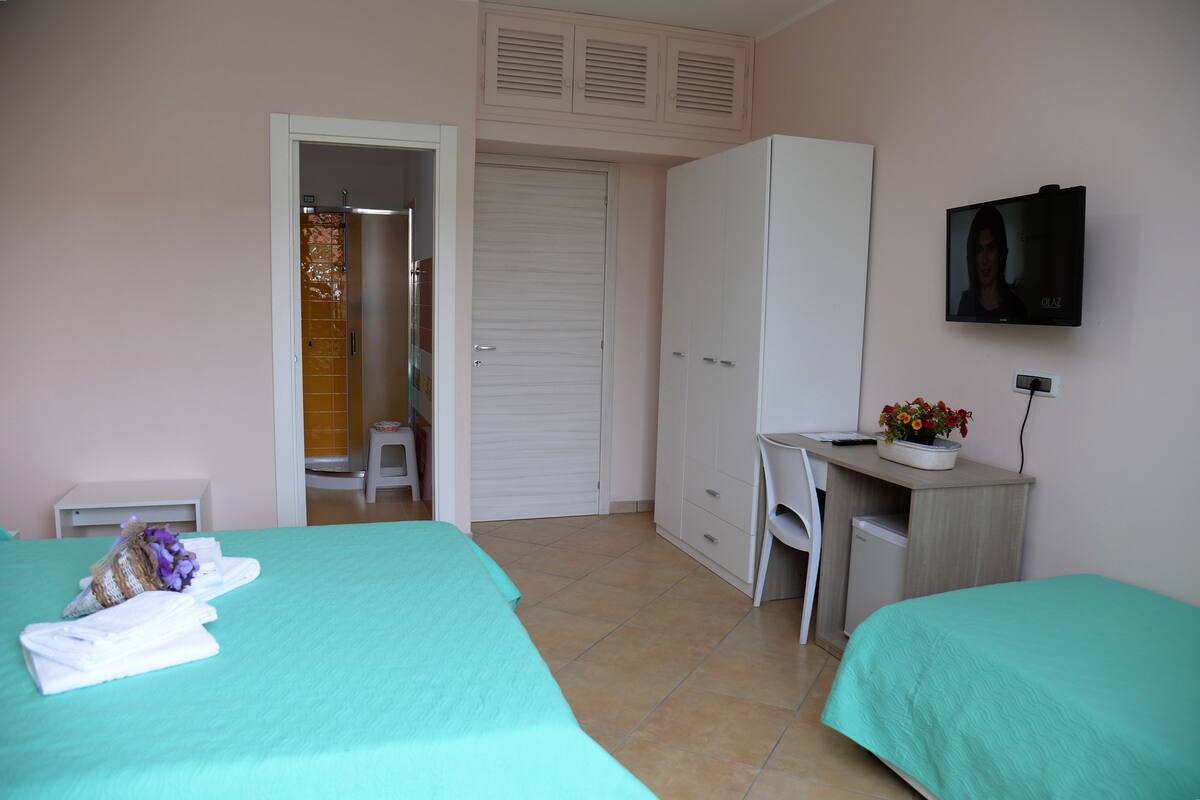Ein Schlafzimmer mit zwei Betten, einem Schreibtisch, einem Kleiderschrank und einem Fernseher an der Wand.