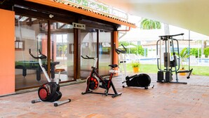 An outdoor gym area with exercise equipment, including stationary bikes and a weight machine, under a covered patio. - Hotel Peñon Suites (Girardot)
