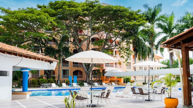 A pool area with lounge chairs, umbrellas, and a building in the background. - Hotel Peñon Suites (Girardot)