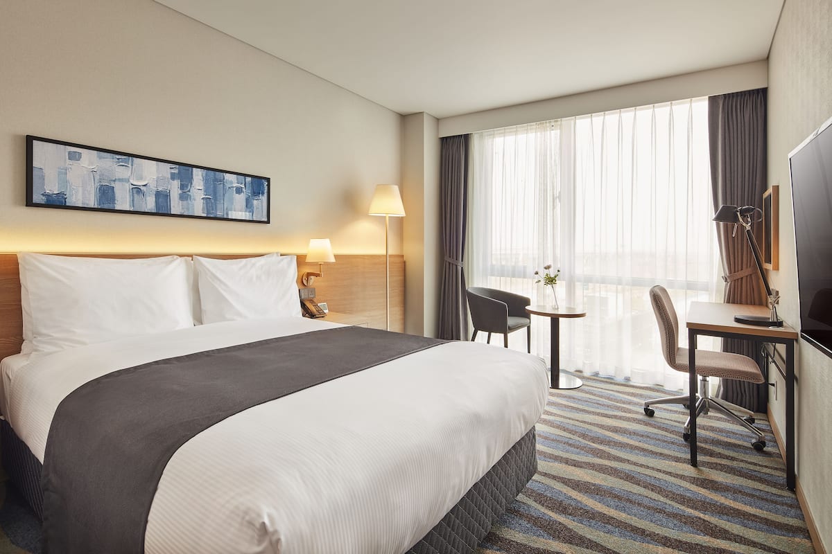 A hotel room with a large bed, a desk with a chair, a TV, and a window with curtains.