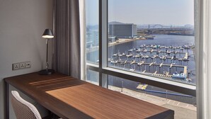 A hotel room with a wooden desk, a lamp, and a view of a marina with boats and a bridge. - Ramada Encore by Wyndham Gimpo Han River Hotel (Gimpo)