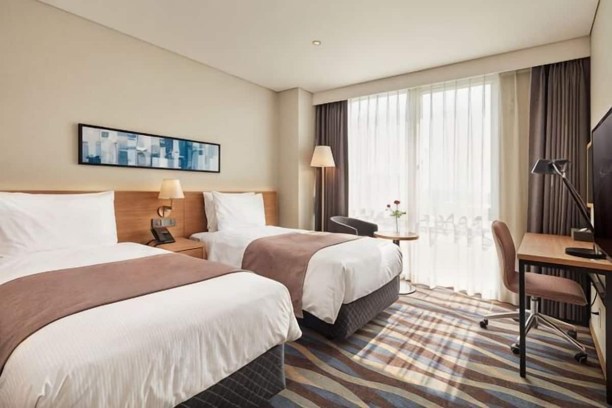 A hotel room with two beds, a desk, a chair, a TV, and a window with curtains.