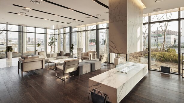 A modern hotel lobby with a marble reception desk, comfortable seating, large windows, and a view of the city. - Ramada Encore by Wyndham Gimpo Han River Hotel (Gimpo)