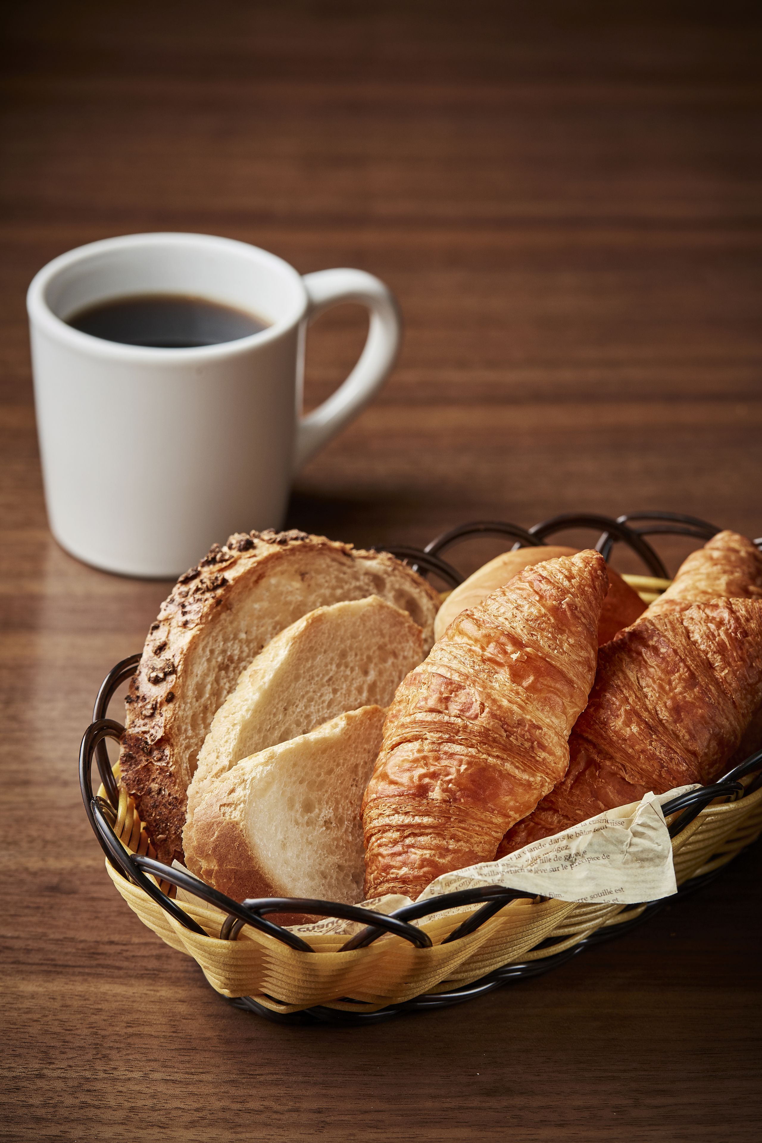 Una cesta de pan y una taza de café sobre una mesa de madera.