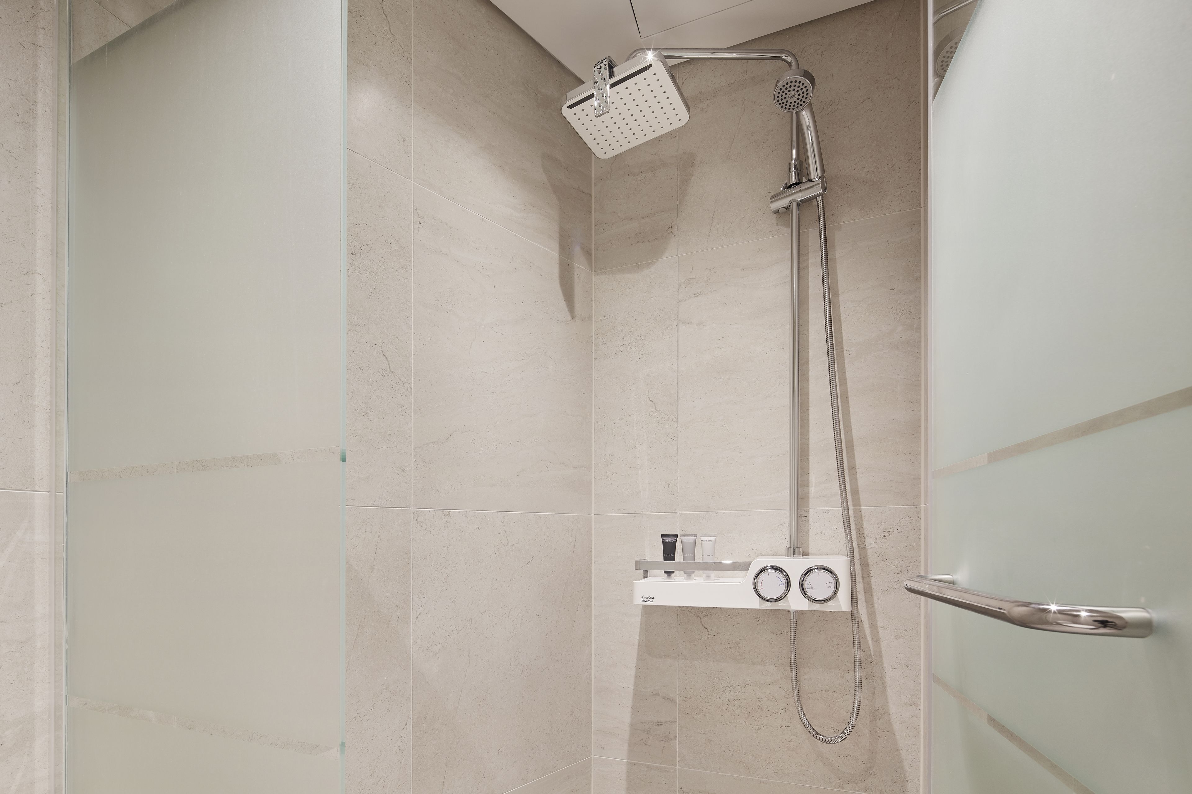 A modern shower with a handheld showerhead and a wall-mounted faucet, a control panel, and a glass door.