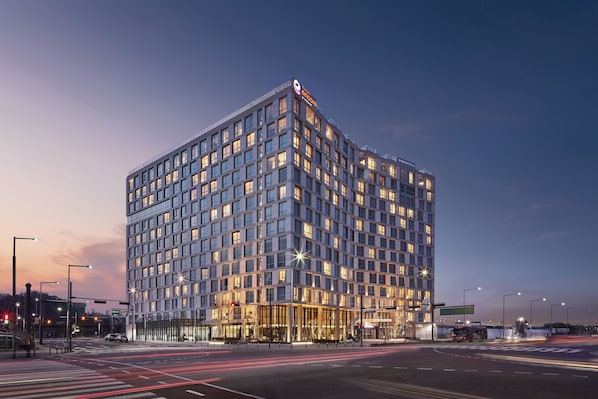 A modern hotel with a glass facade, multiple floors, and a prominent signage at the top.