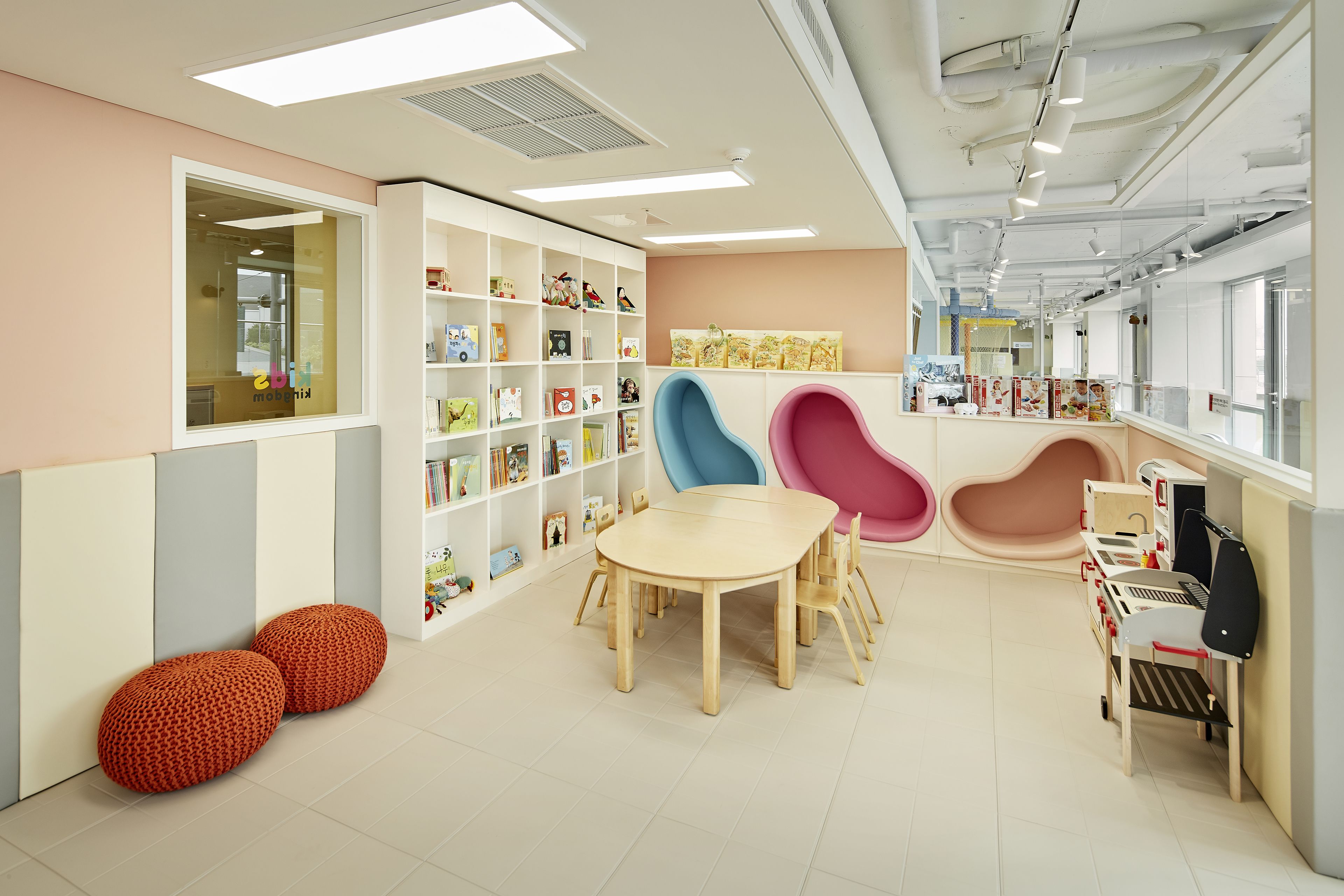 Uma sala de brinquedos infantil moderna, com uma mesa redonda, cadeiras coloridas e uma estante cheia de brinquedos e livros.