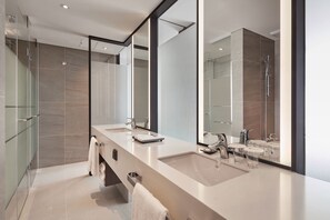 A modern bathroom with a large mirror, two sinks, and a shower.