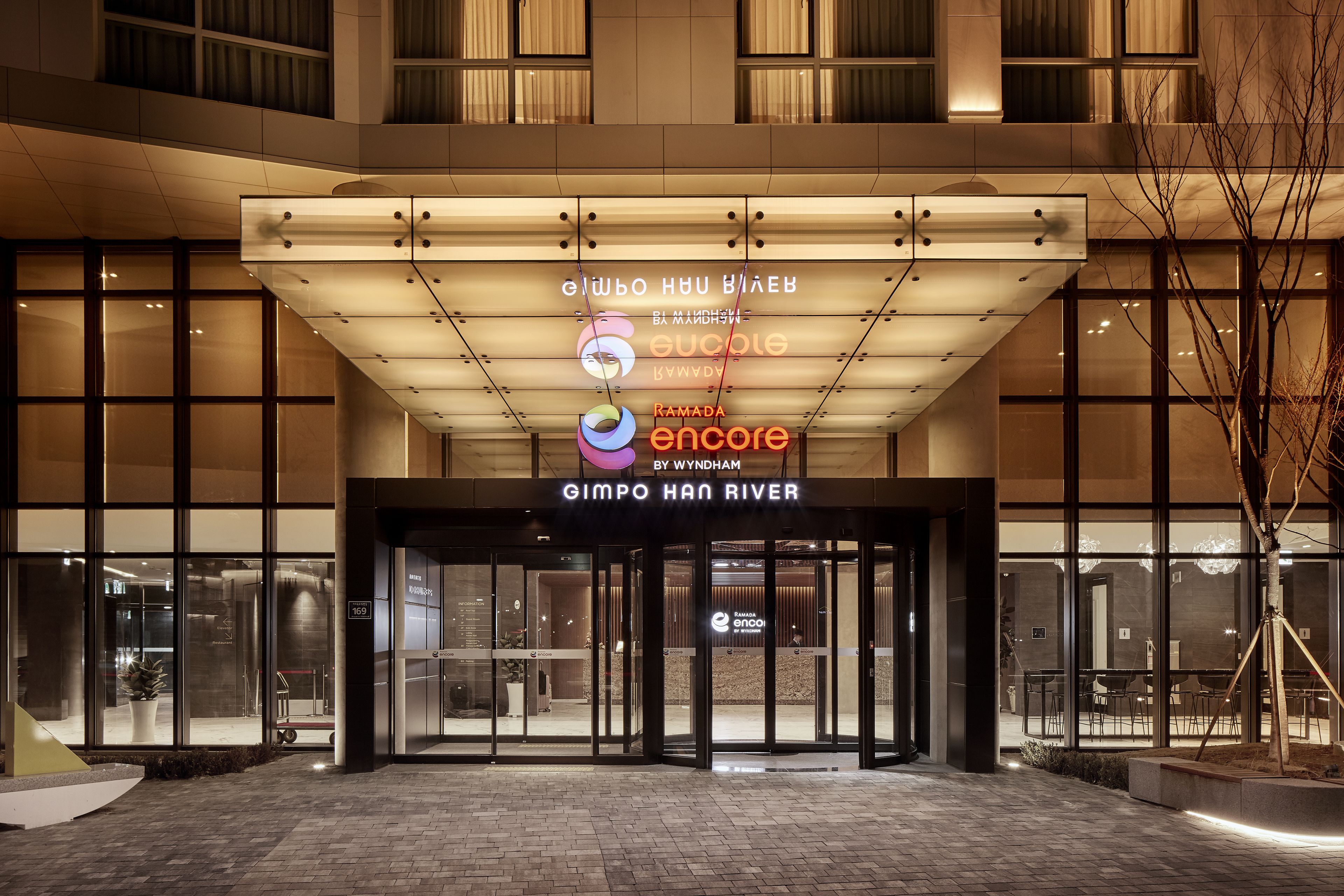 A hotel entrance with a modern design, featuring a large illuminated sign and glass doors.