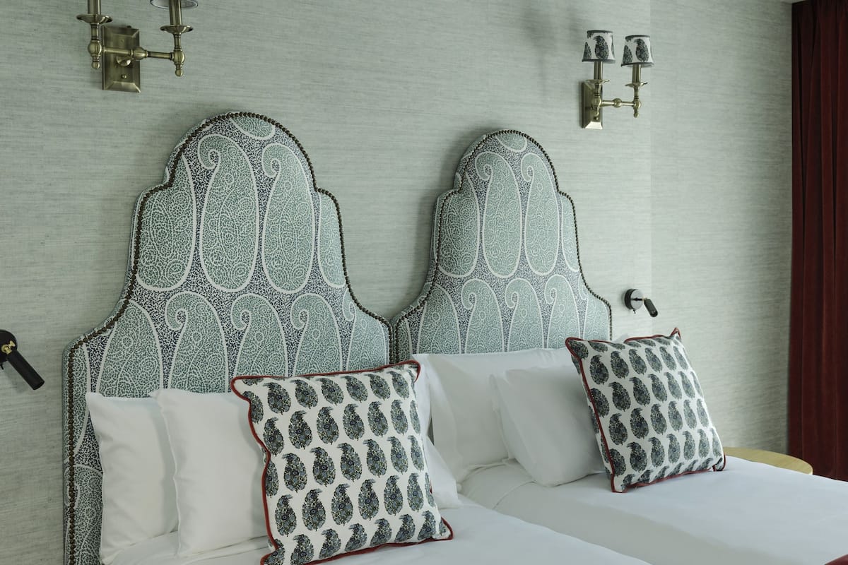 A double bed with patterned pillows, a red throw blanket, and a headboard with a paisley design.