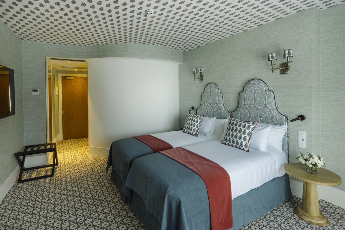 A hotel room with a large bed, a bedside table, a wall-mounted lamp, and a patterned floor.