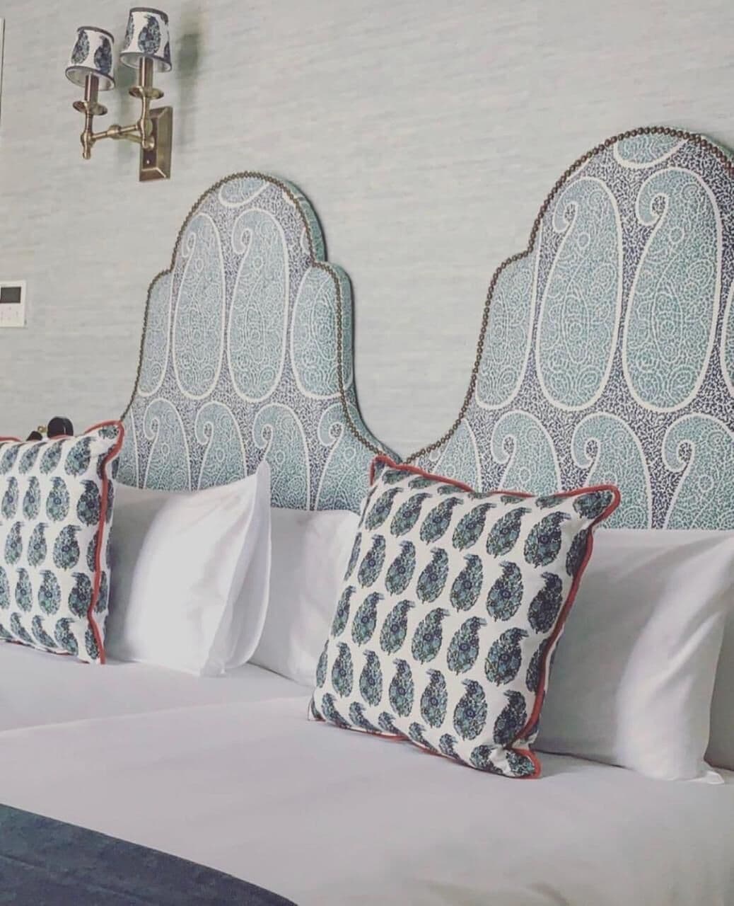 A bed with a patterned headboard and decorative wall sconces.