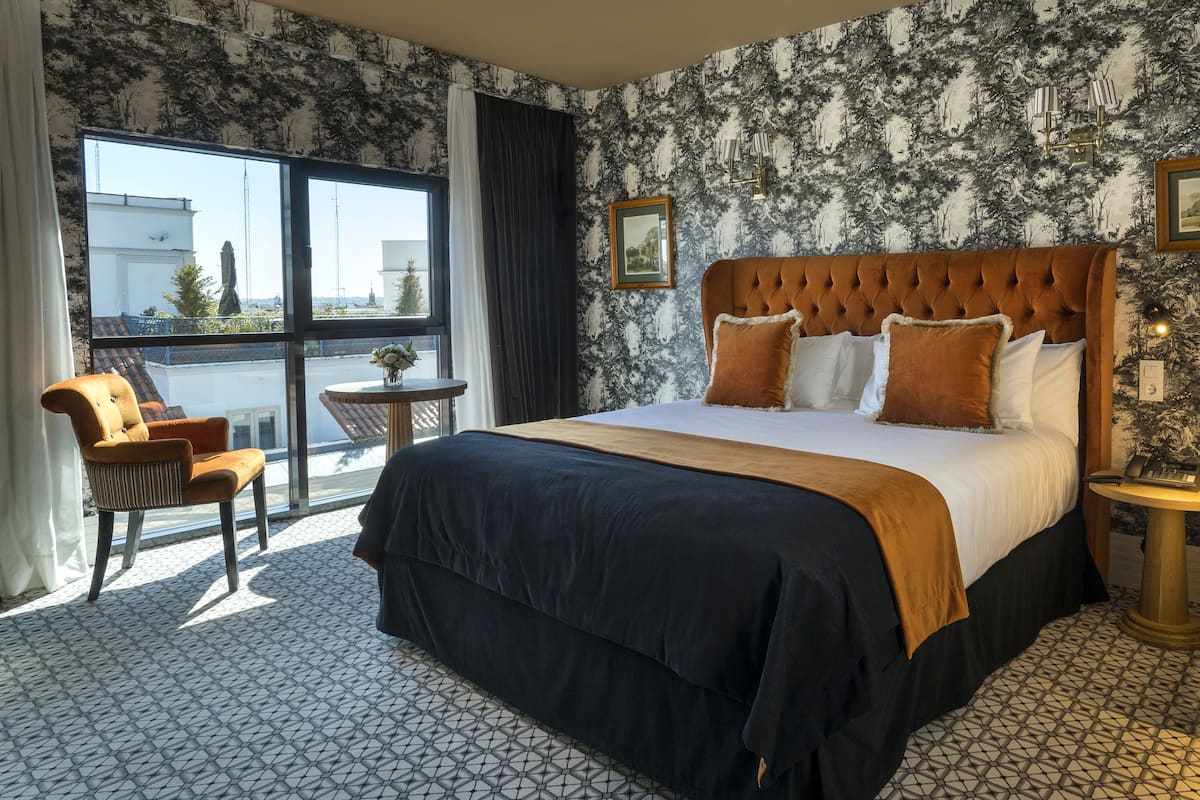 A hotel room with a large bed, a chair, a small table, and a view of the outside.