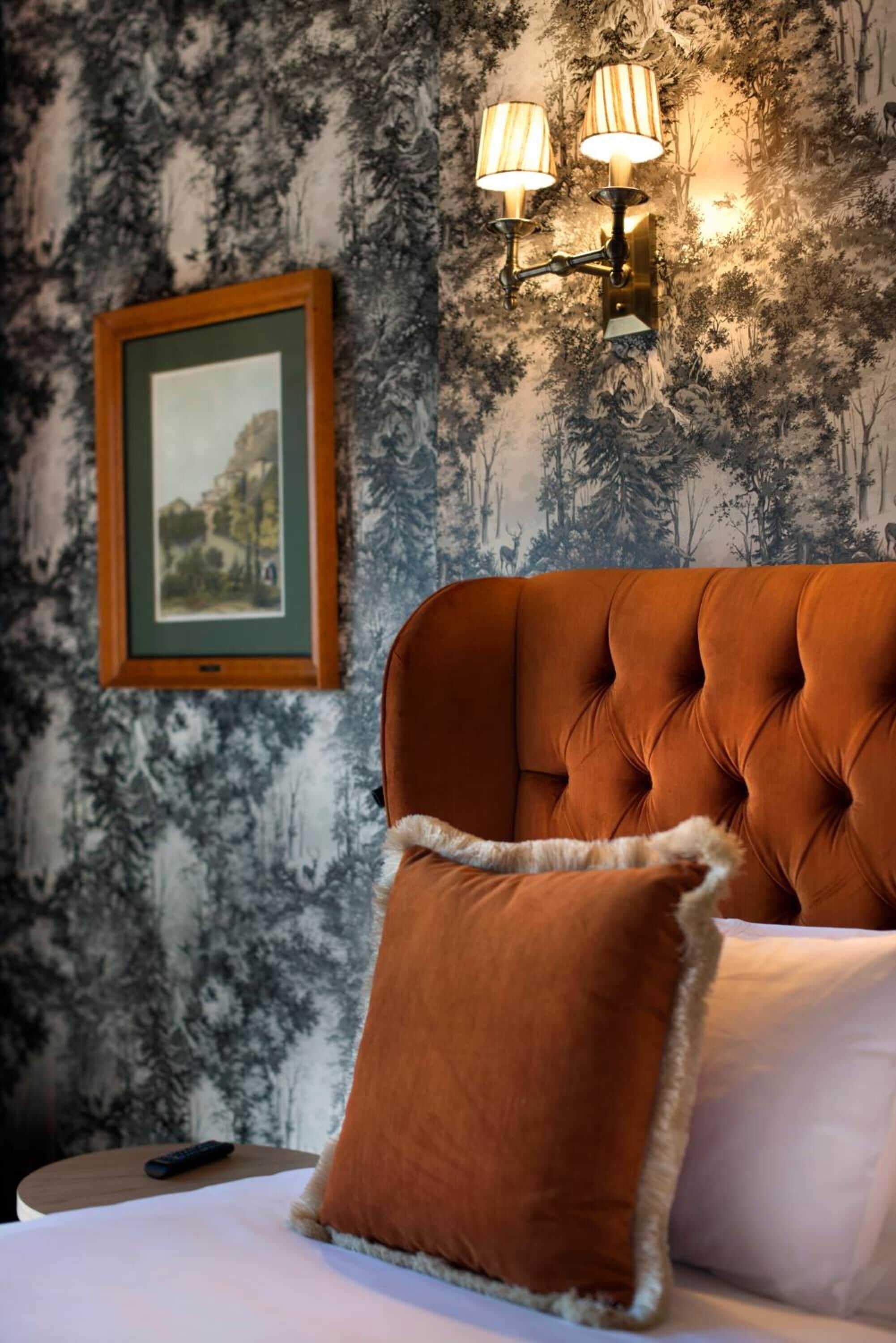 A bedroom with a tufted headboard, a framed picture on the wall, and a wall-mounted lamp.