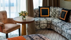 Habitació d'hotel amb un sofà estampat, una taula rodona de fusta amb un ram de flors, i una catifa amb dibuixos.