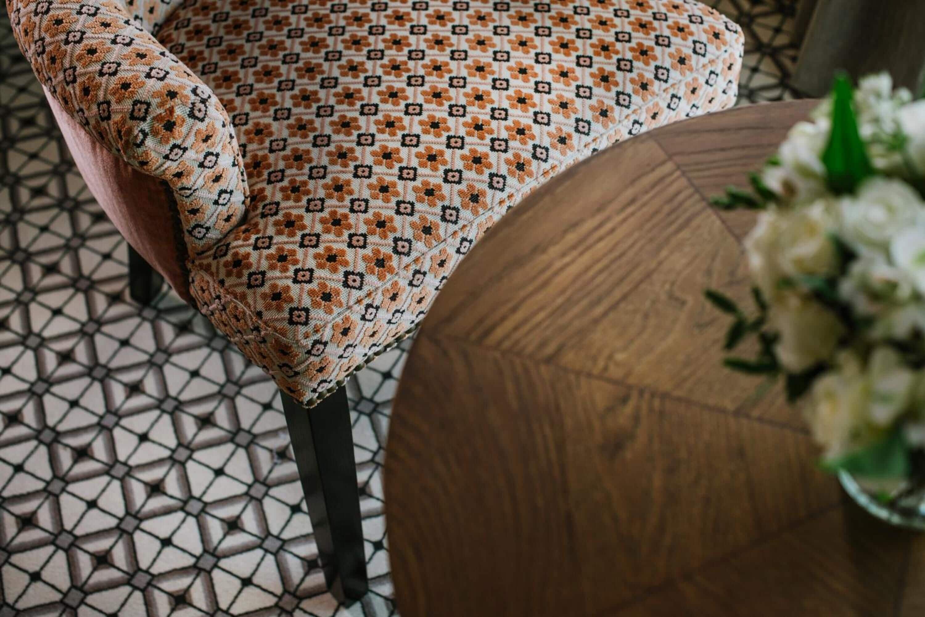 Una silla con tela estampada, una mesa de madera y un piso de baldosas.