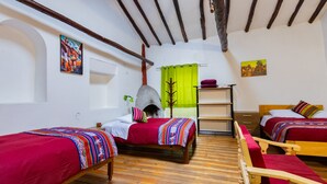 A room with two wooden beds with red bedding, a wooden chair, a fireplace, and a green curtain. - Tucan Hostel (Cusco)