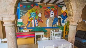 A dining area with a mural, white chairs, and a table. - Tucan Hostel (Cusco)