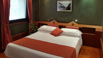 Camera d'albergo con un letto, una testiera in legno, un comodino, una lampada a parete e un quadro incorniciato.