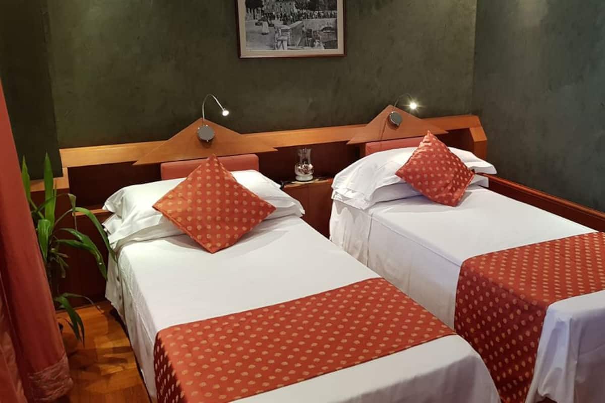A hotel room with two single beds, each with a red polka dot bedspread and matching pillows. There is a wooden headboard, a bedside table with a lamp, and a framed picture on the wall.